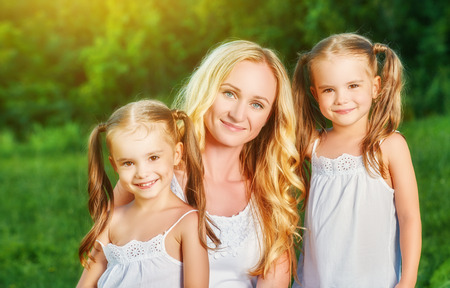 happy family mother and children twin sisters on meadow in the summer on a green grassの写真素材