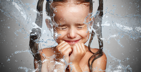 happy funny child girl in a spray of water droplets laughsの写真素材