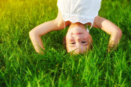 happy child girl standing upside down on his head on the grass in the summerの写真素材