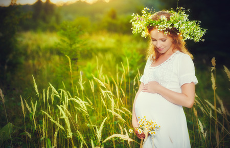beautiful pregnant woman in wreath  relaxing in the summer nature meadow with sunsetの写真素材