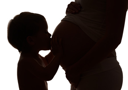 Happy family. Silhouette  of happy child kissing  belly of pregnant motherの写真素材