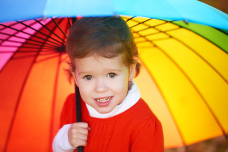 Beautiful little child girl with multicolored rainbow umbrella on nature in the parkの写真素材