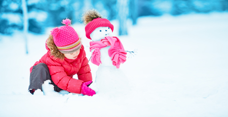 happy child girl with a snowman on a snowy winter walkの写真素材