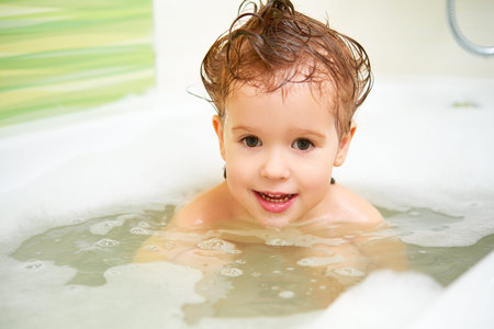 happy child toddler girl bathes in a bath with foam and bubbles