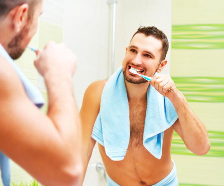 man brushing his teeth with toothbrush in morning of mirror in bathroomの写真素材