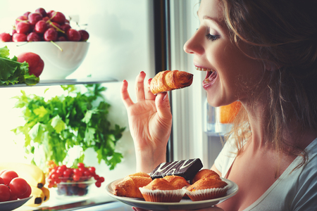 woman eats sweets at night to sneak in a refrigeratorの写真素材