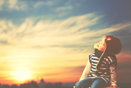 Happy child dreams of becoming a pilot aviator on sky sunsetの写真素材