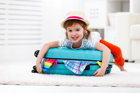 happy child girl tourist packs clothes into a suitcase for travel, vacationの写真素材