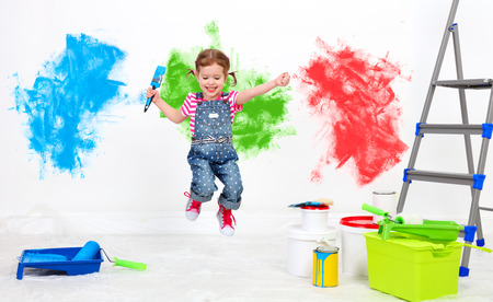 happy funny child girl doing repairs, jumping and paint the wall at homeの写真素材