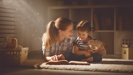 happy family mother and daughter read a book in the evening at home