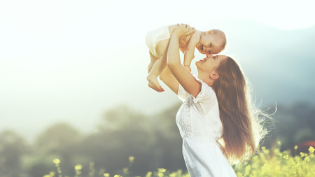 happy harmonious family outdoors. mother throws baby up, laughing and playing in the summer on the natureの写真素材