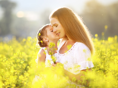 Happy family on a summer meadow. little girl child daughter hugging and kissing motherの写真素材