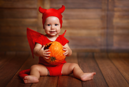 funny baby in devil halloween costume with pumpkin on a dark wooden backgroundの写真素材