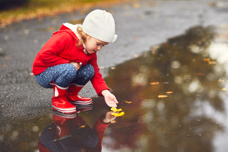 happy child girl playing with autumn leaves in a puddle after a rain in autumnの写真素材