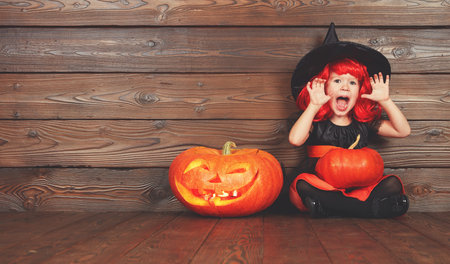 funny child girl in witch costume for Halloween with pumpkin Jack on a dark wooden backgroundの写真素材