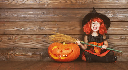 funny child girl in witch costume for Halloween with pumpkin Jack on a dark wooden backgroundの写真素材