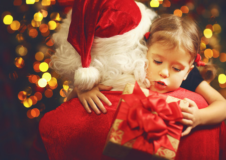 happy child girl hugging Santa and holding a giftの写真素材