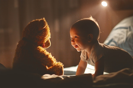 Happy baby laughing with teddy bear in bed in the darkの写真素材