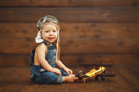 funny baby boy pilot aviator with airplane laughing on wooden backgroundの写真素材
