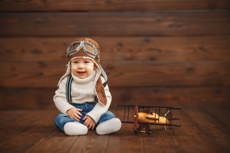funny baby boy pilot aviator with airplane laughing on wooden backgroundの写真素材