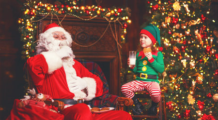 Santa Claus and a elf child in a Christmas drinking milk and eating cookiesの写真素材