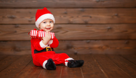 Happy baby in a Christmas costume Santa Claus with gifts on wooden background