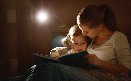 mother and child girl reading a book in bed before going to sleepの写真素材