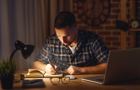 young man working on the computer at home at night in the darkの写真素材