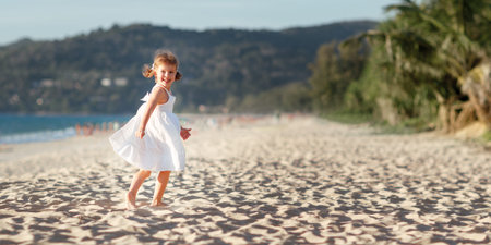 Happy child girl in a white dress running on the beach by the sea in summerの写真素材