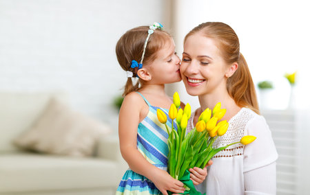 Happy mother's day! Child daughter congratulates moms and gives her a postcard and flowers tulipsの写真素材