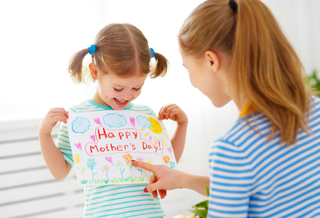 Happy mother's day! Child daughter congratulates moms and gives her a postcard and flowers tulipsの写真素材