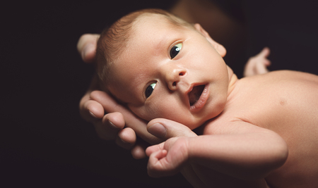Newborn baby in his father's hands in the dark on a black backgroundの写真素材