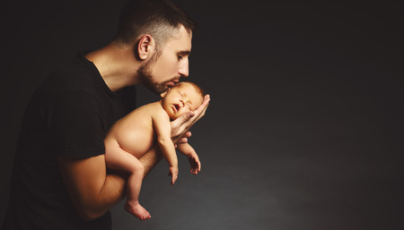 Newborn baby in his father's hands in the dark on a black backgroundの写真素材