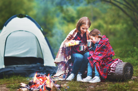 Family mother and child daughter drinking tea  on a camping trip with a tent and by the bonfireの写真素材