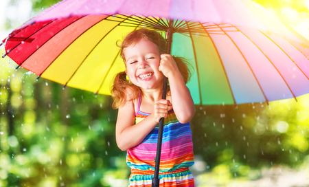 Happy child girl laughs and plays under the summer rain with an umbrellaの写真素材