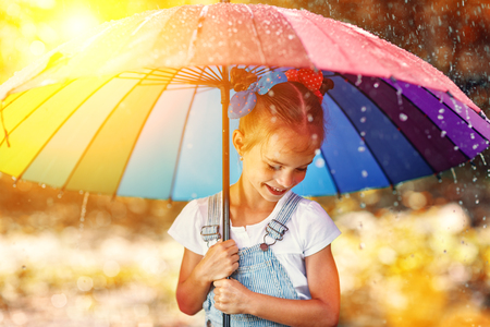 Happy funny ba child by girl with a multicolored umbrella jumping on puddles in rubber boots and laughingの写真素材
