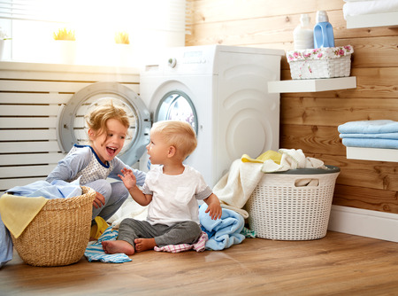 Happy children boy and girl in   in the laundry load a washing machineの写真素材