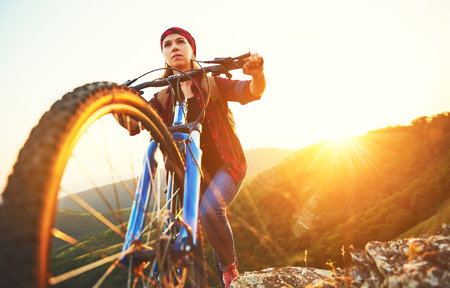 Woman tourist on a bicycle at the top of the mountain at sunset outdoors during a hike in summerの写真素材