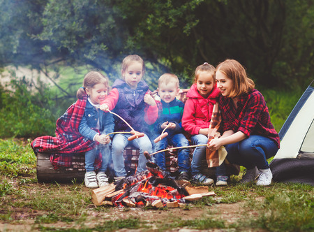 Happy tourist family on a journey hike. mother and children fry sausages on bonfire near the tentの写真素材