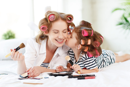 Happy family mother and baby daughter in curlers  doing makeup on bedの写真素材