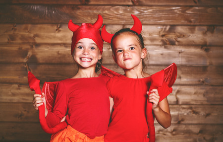 holiday halloween. funny funny sisters twins children in carnival costumes devil  on a wooden backgroundの写真素材