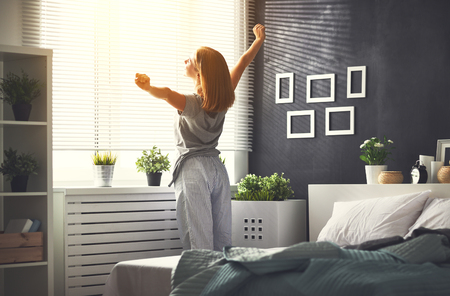 young happy woman woke up in the morning in the bedroom by the window with her backの写真素材