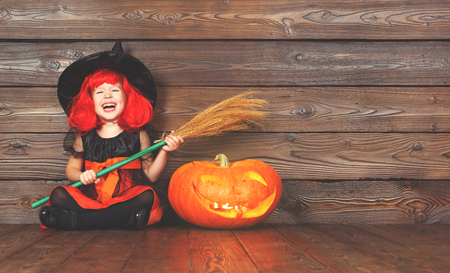 happy child girl in costume witch for Halloween with pumpkins with burning eyes on   wooden background