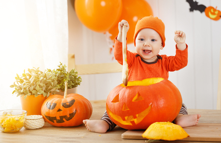 baby cut a pumpkin for Halloween in the kitchen at homeの写真素材
