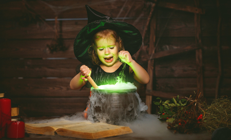Halloween. little witch child cooking potion in the cauldron with spell bookの写真素材