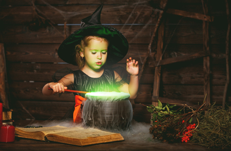 Halloween. little witch child cooking potion in the cauldron with spell bookの写真素材