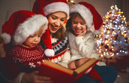 happy family mother and children read a book at christmas near   fireplace at homeの写真素材