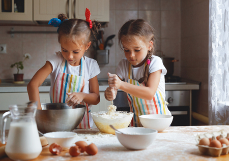 happy sisters children girls bake cookies, knead dough, play with flour and laugh in the kitchen
の写真素材