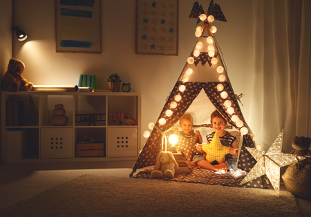 happy family loving children brother and sister play, laugh and hug   in dark tent in playroom at home
の写真素材