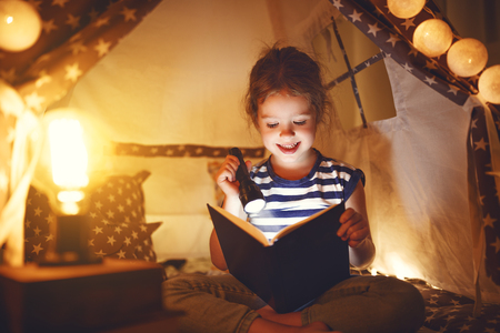happy child girl laughing and reading book in dark in a tent at home
の写真素材